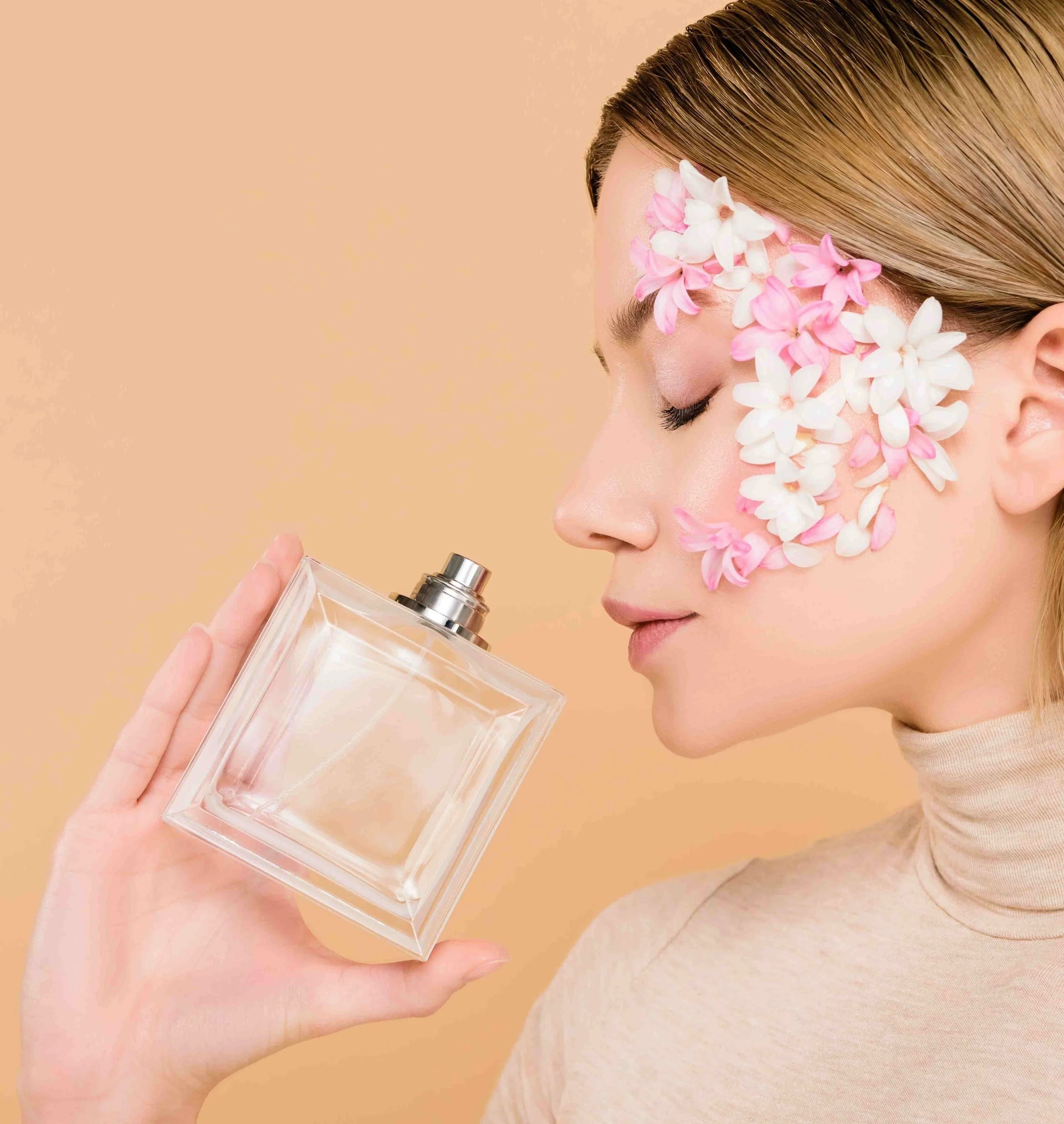 Woman holding perfume bottle with floral decorations on face, soft peach background