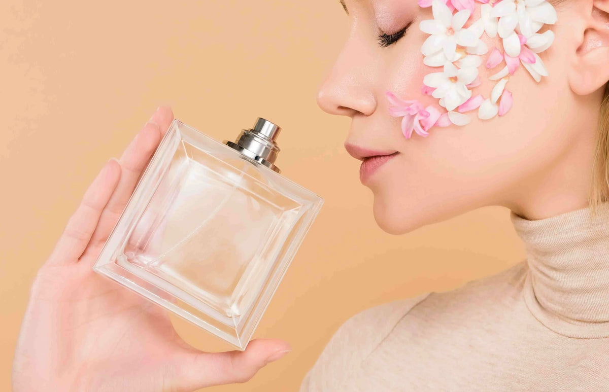 Woman holding perfume bottle near face with pink and white flowers on cheek