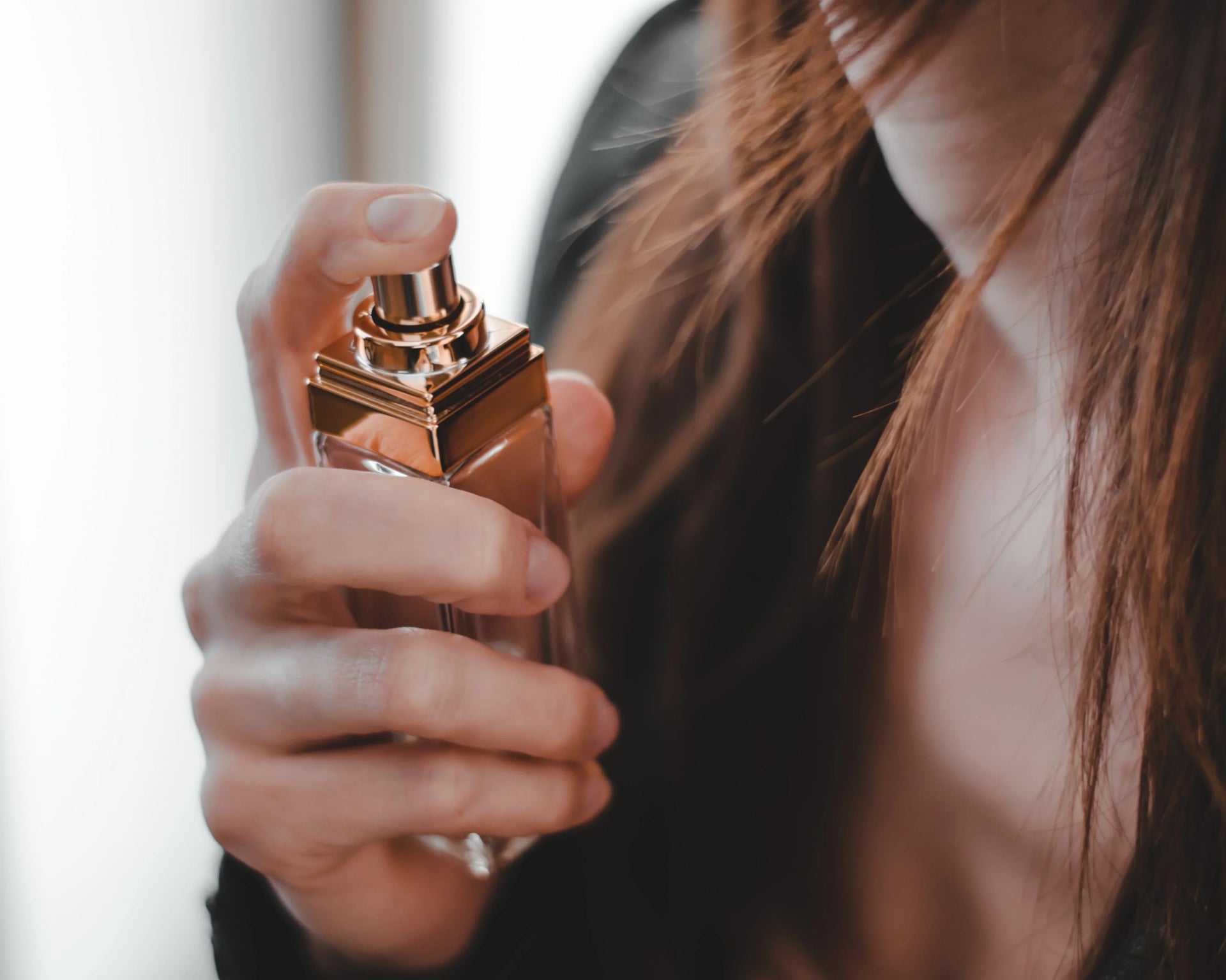 Woman spraying luxury perfume on neck, closeup of elegant glass perfume bottle